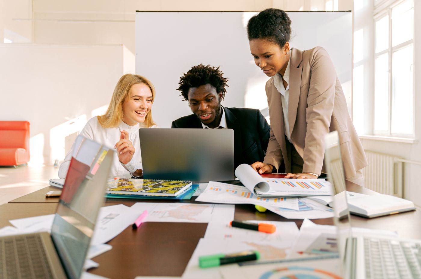 Three coworkers looking at a laptop in a small office.